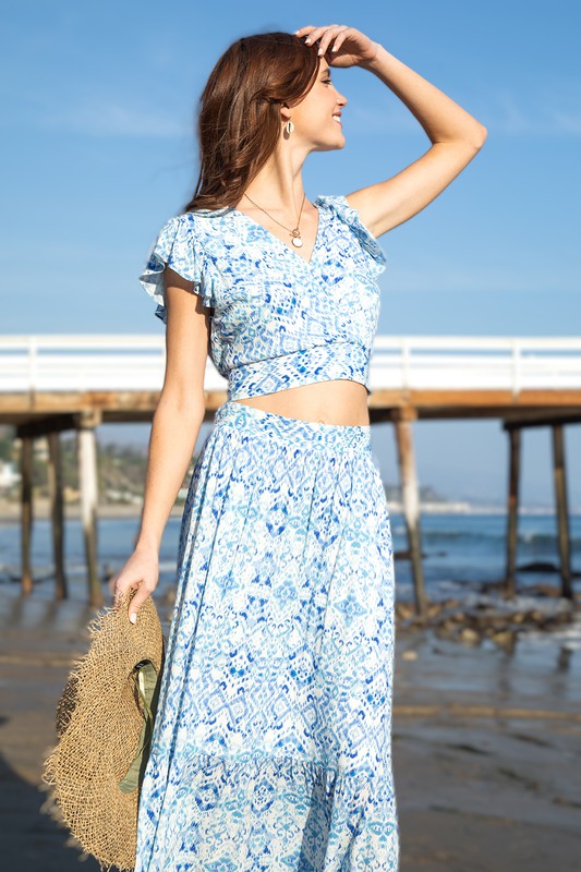 A model is wearing a blue and white skirt set. The top has a crop top and the skirt is midi length. The model is at Pismo Beach California
