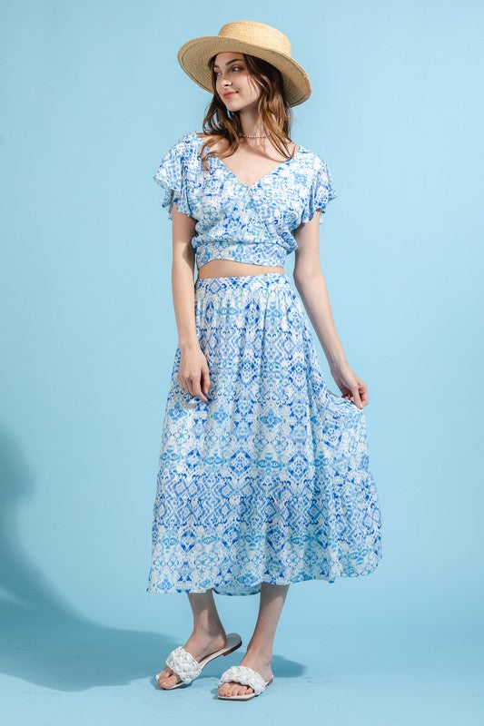 A model is wearing a blue and white skirt set. The top has a crop top and the skirt is midi length.