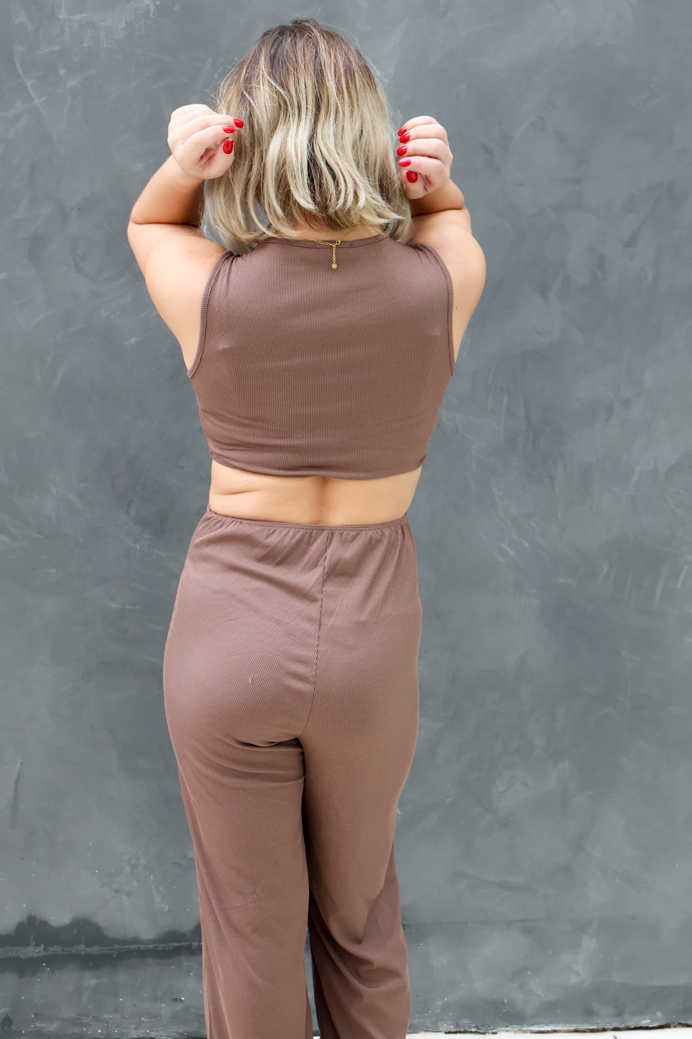 Person wearing a brown sleeveless top and pants against a gray wall