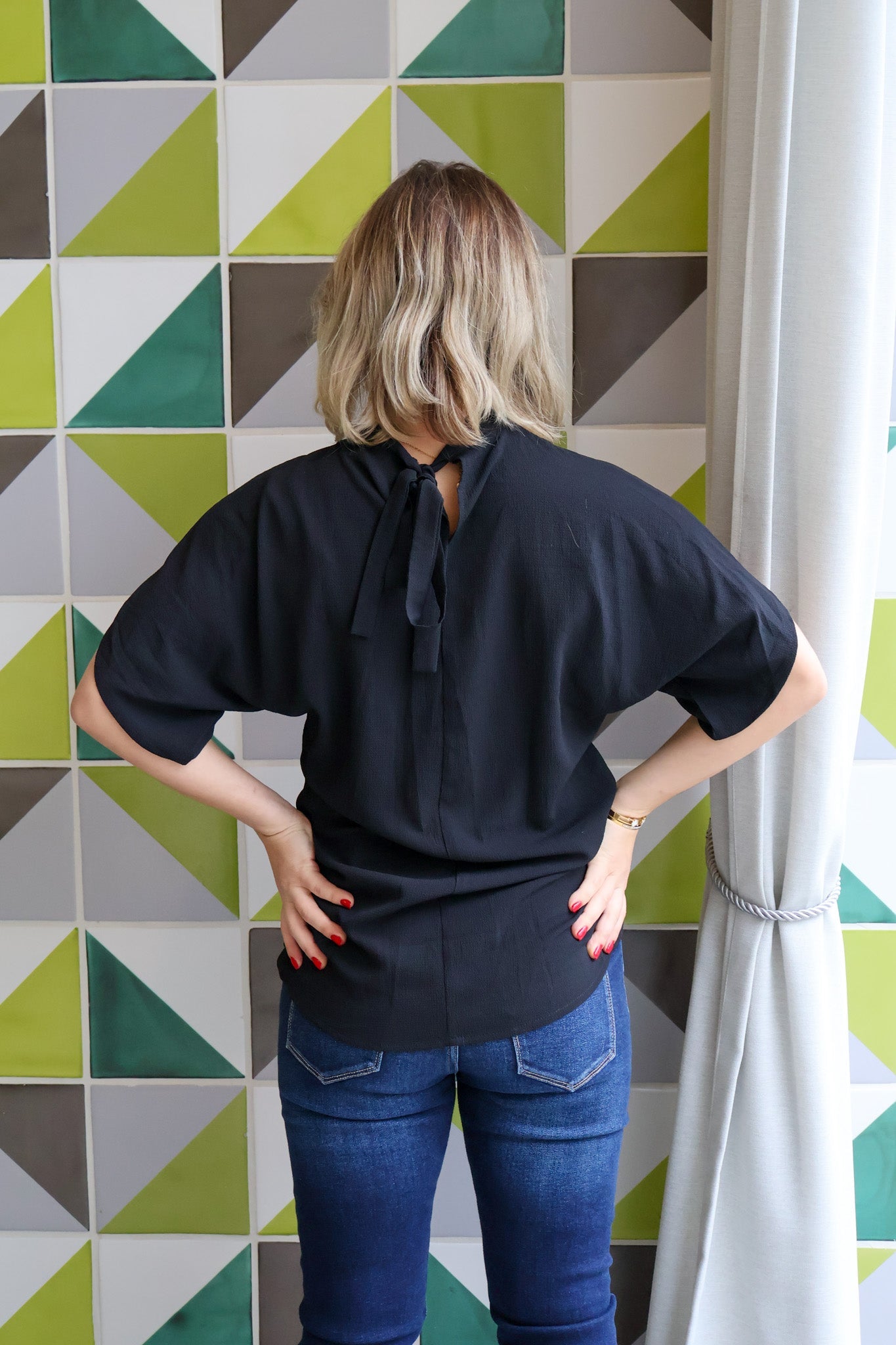 Person wearing a black top and blue jeans standing in front of a geometric patterned wall.