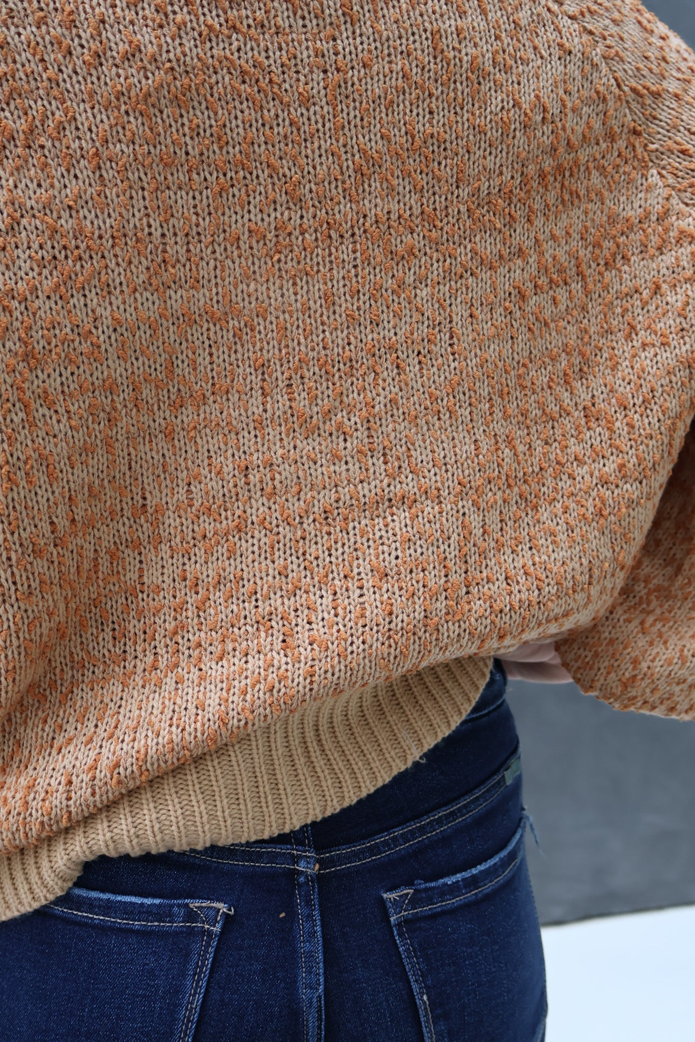 Close-up of a person wearing a brown sweater and blue jeans with a blurred background.