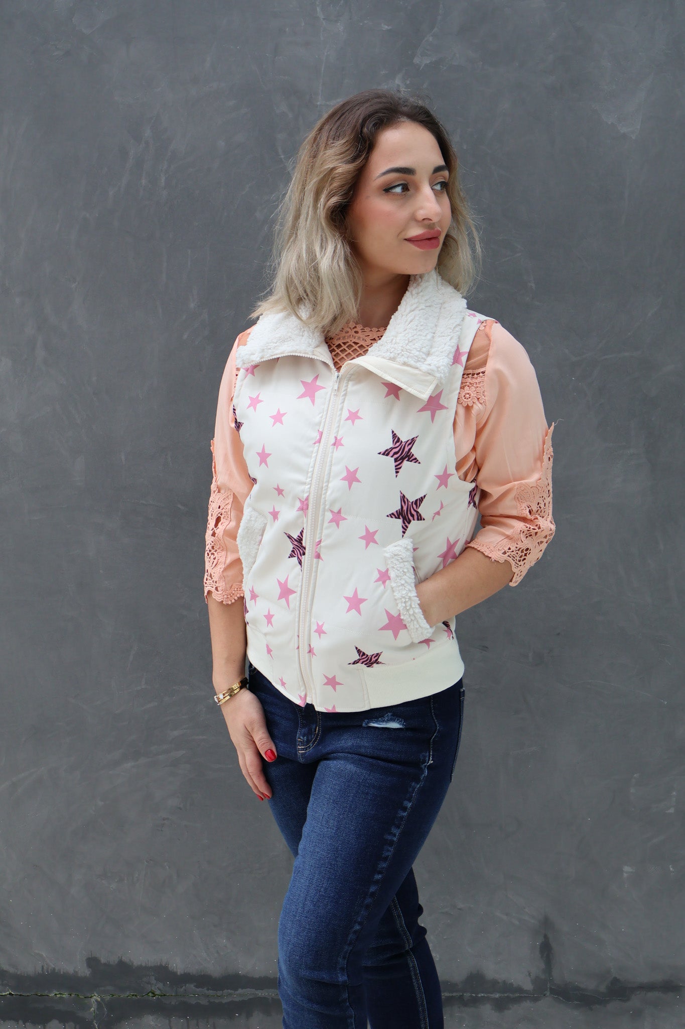Woman wearing a white puffer vest with pink star patterns against a gray background