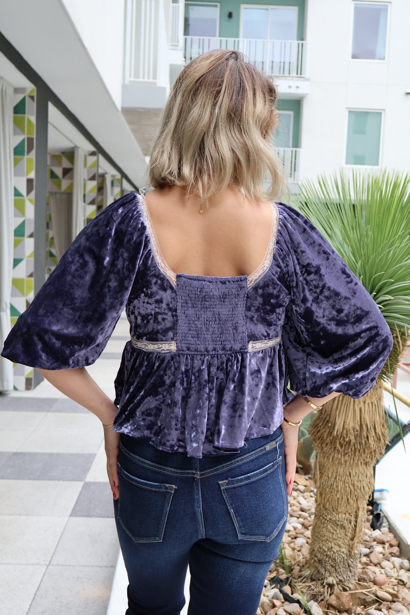 Person wearing a purple velvet top and blue jeans standing in an outdoor setting.