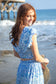 A model is wearing a blue and white skirt set. The top has a crop top and the skirt is midi length. The model is at Pismo Beach California
