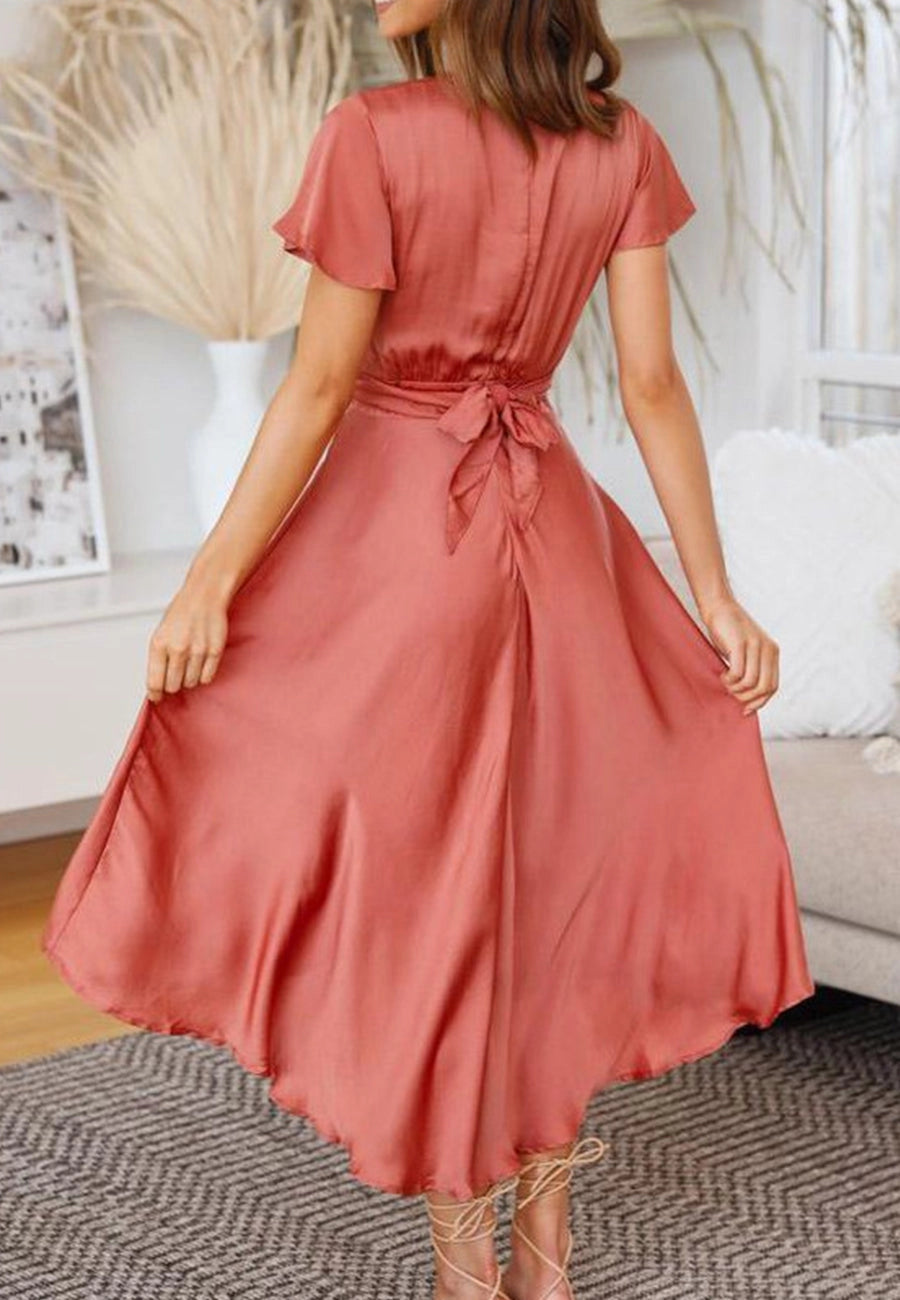 Features a twist style, bow detail, flutter sleeves, asymmetrical hem, and knee length