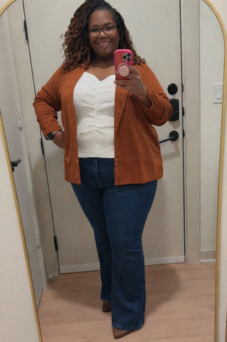 Person wearing a brown cardigan, white top, and blue jeans taking a mirror selfie.