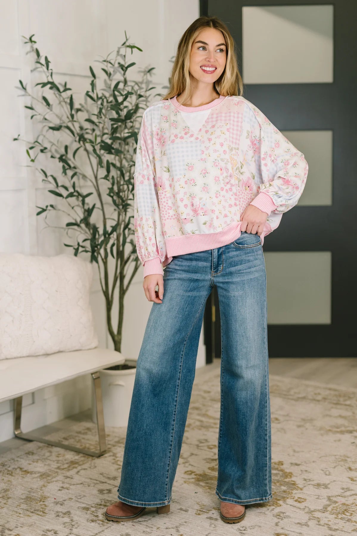 Woman wearing a floral blouse and blue jeans standing in a living room.