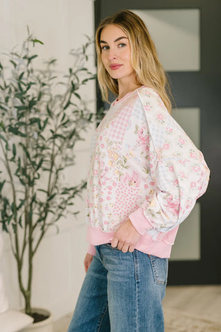 Woman wearing a floral blouse and jeans standing indoors with a plant in the background