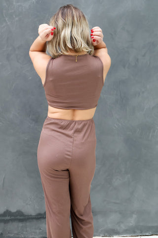 Person wearing a brown sleeveless top and pants against a gray wall