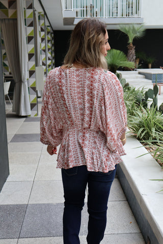 Woman wearing a patterned blouse and dark jeans walking outdoors.