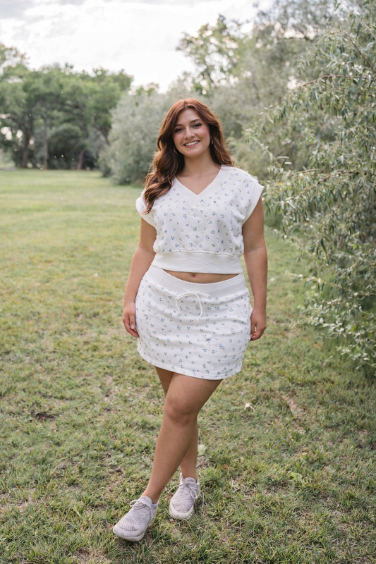 Woman in a white outfit standing in a grassy field with trees in the background