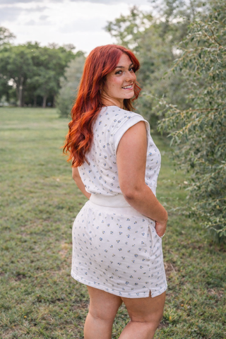 Woman in a white dress standing in a grassy field with trees in the background