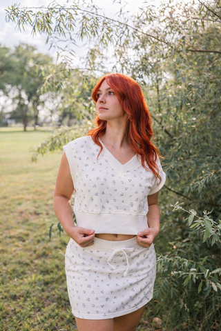 Woman with red hair wearing a white outfit standing in a natural setting