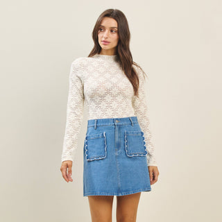 Woman wearing a white lace top and blue denim skirt on a plain background