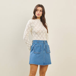 Woman wearing a white lace top and blue denim skirt against a plain background
