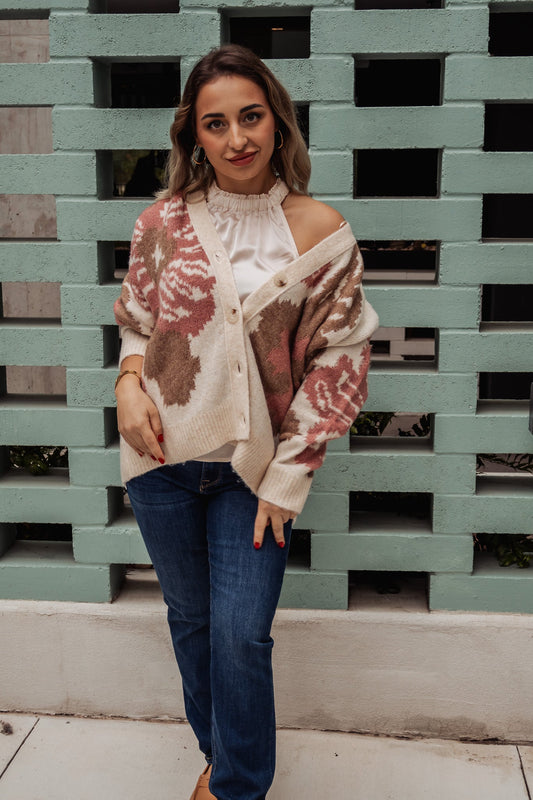 Woman wearing a patterned sweater and jeans standing in front of a textured wall.