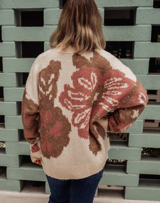 Person wearing a floral-patterned sweater standing in front of green pallets