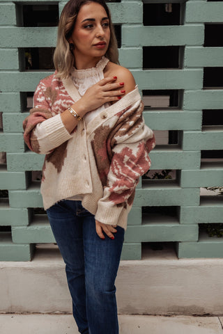 Woman wearing a patterned sweater and jeans against a green brick wall.