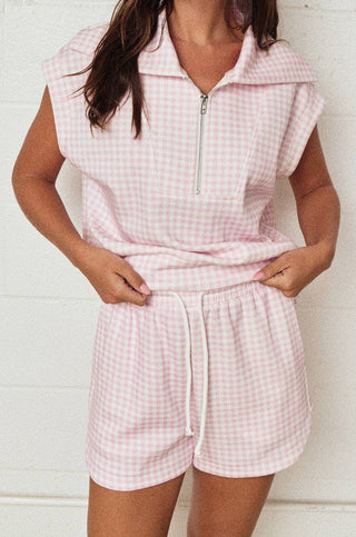 Woman wearing a pink checkered outfit against a white brick wall