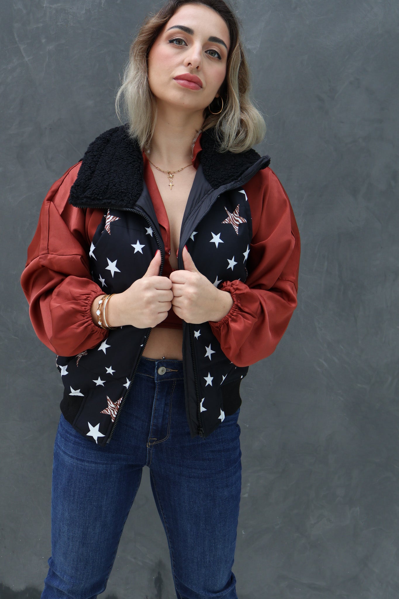 Woman wearing a red jacket with a black vest over it against a gray background