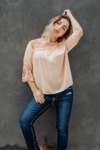 Woman wearing a light pink blouse with lace details and blue jeans against a gray background