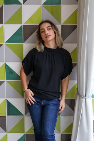 Woman wearing a black top and blue jeans standing against a geometric-patterned wall.