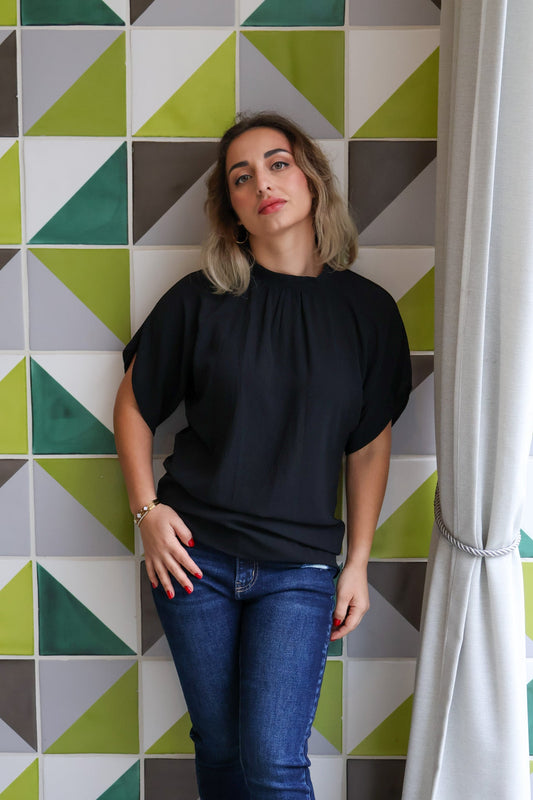 Woman wearing a black top and blue jeans standing against a geometric-patterned wall.