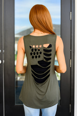 Woman wearing a sleeveless green top with a black graphic design, standing in front of a glass door.