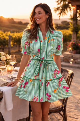 Woman in a green dress with floral patterns standing outdoors near a table with wine glasses.