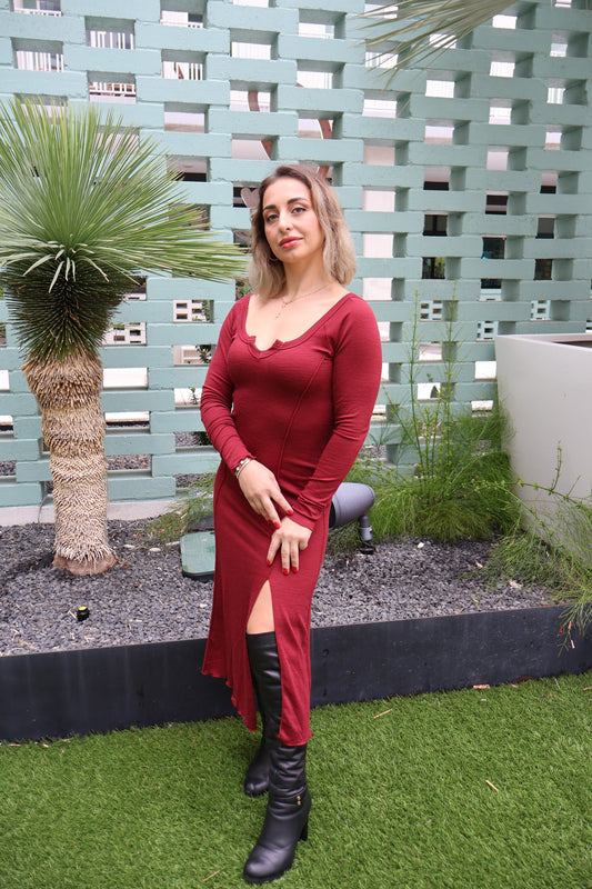 Woman in a red dress and black boots standing in a garden with a green fence and plants.