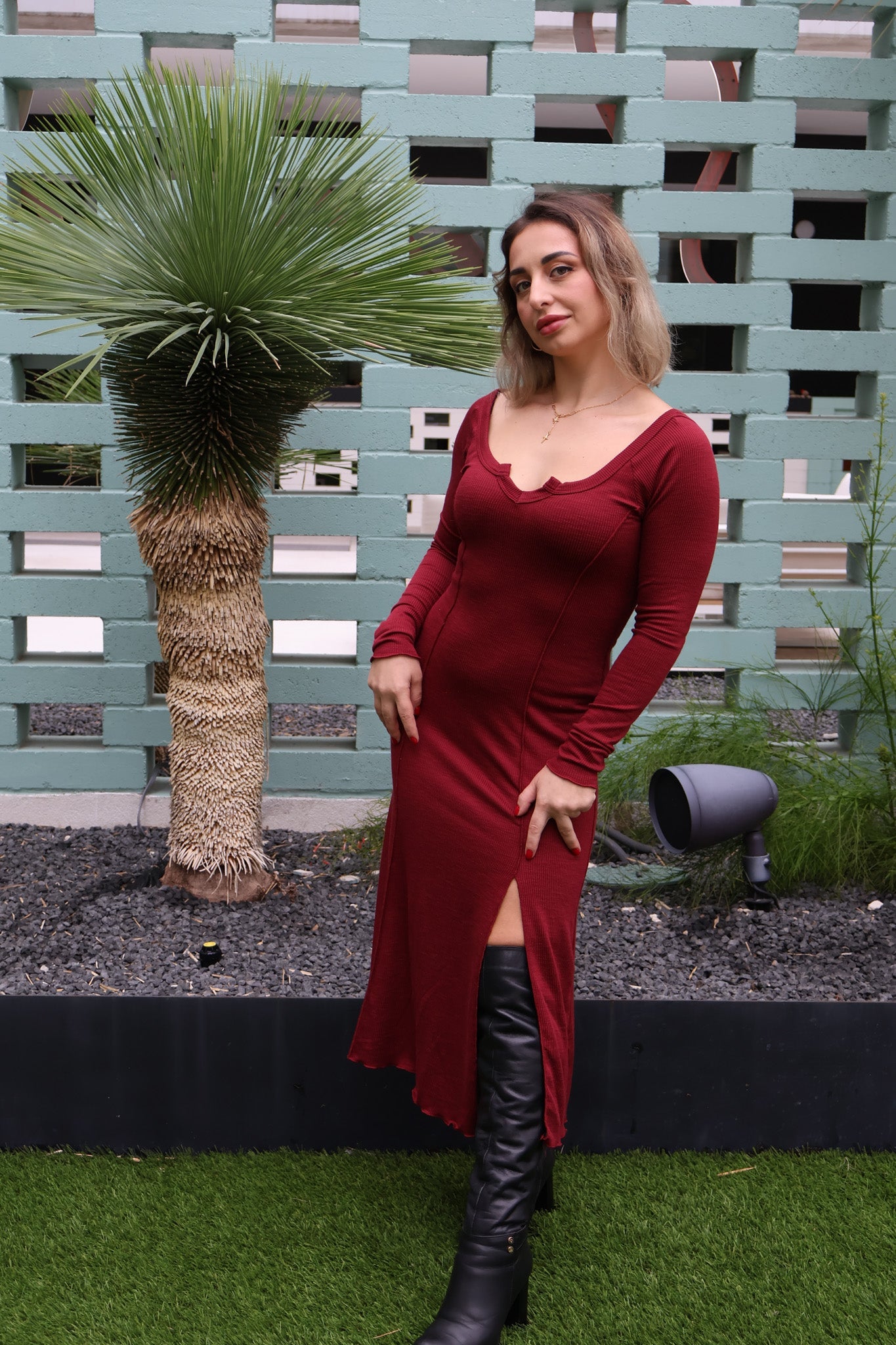 Woman in a red dress with a high slit standing in front of a textured wall.