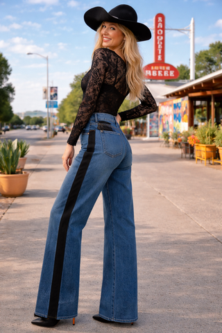 Woman in high-waisted blue jeans and black lace top with a cowboy hat on a street.