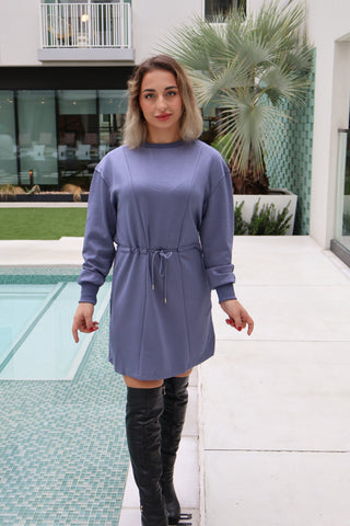 Woman in a steel blue dress and black knee-high boots standing by a pool.