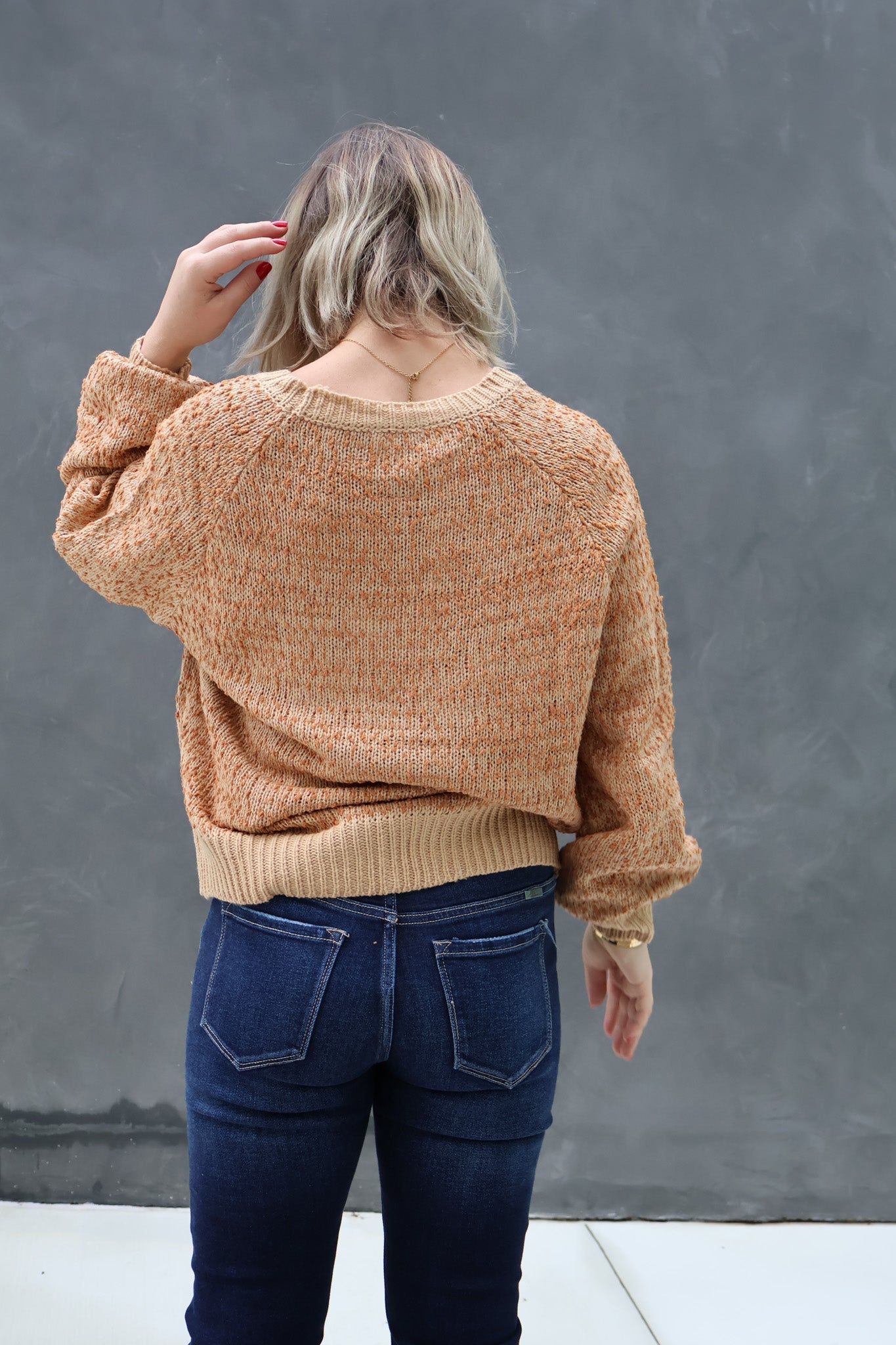 Person wearing a brown sweater and blue jeans against a gray background