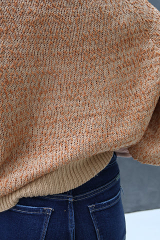 Close-up of a person wearing a brown sweater and blue jeans with a blurred background.