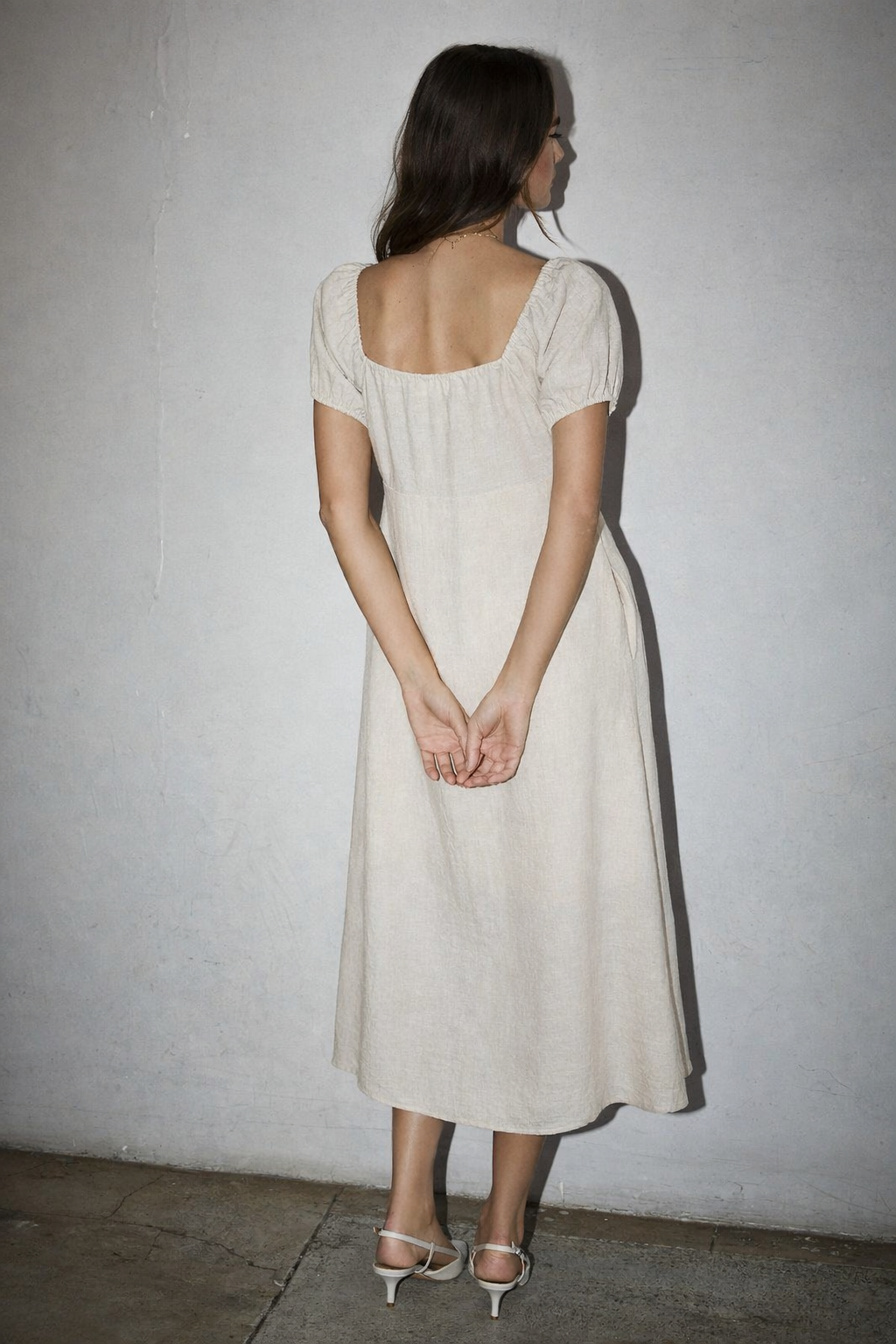 Woman wearing a beige dress against a plain wall