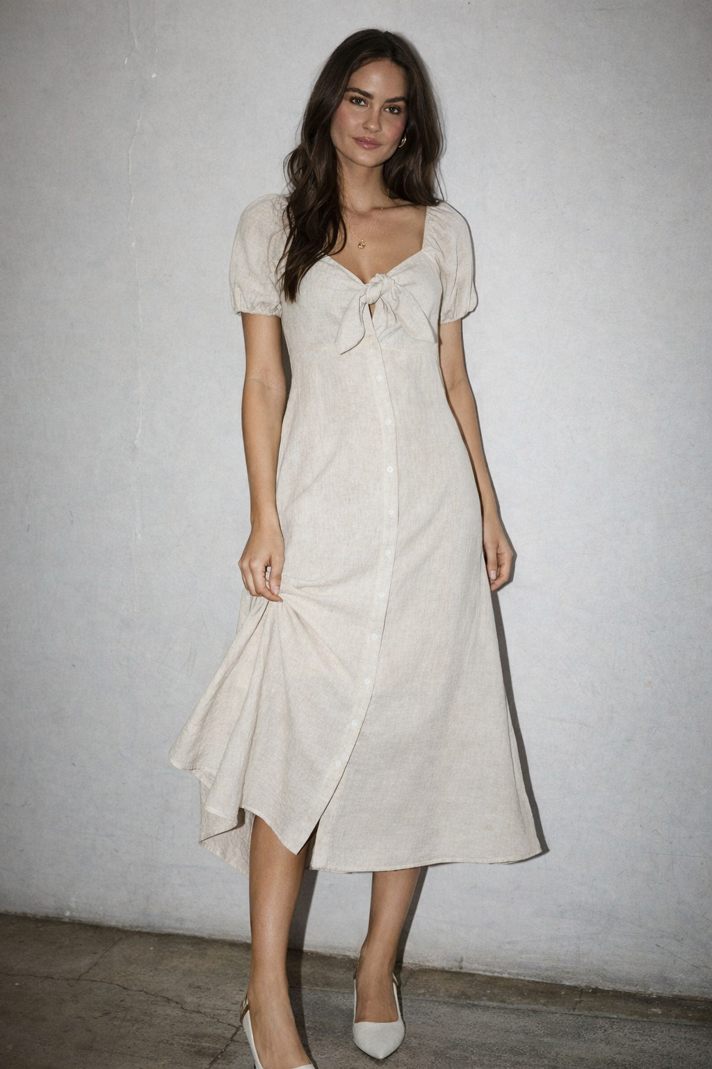 Woman wearing a white dress with a bow detail against a plain background