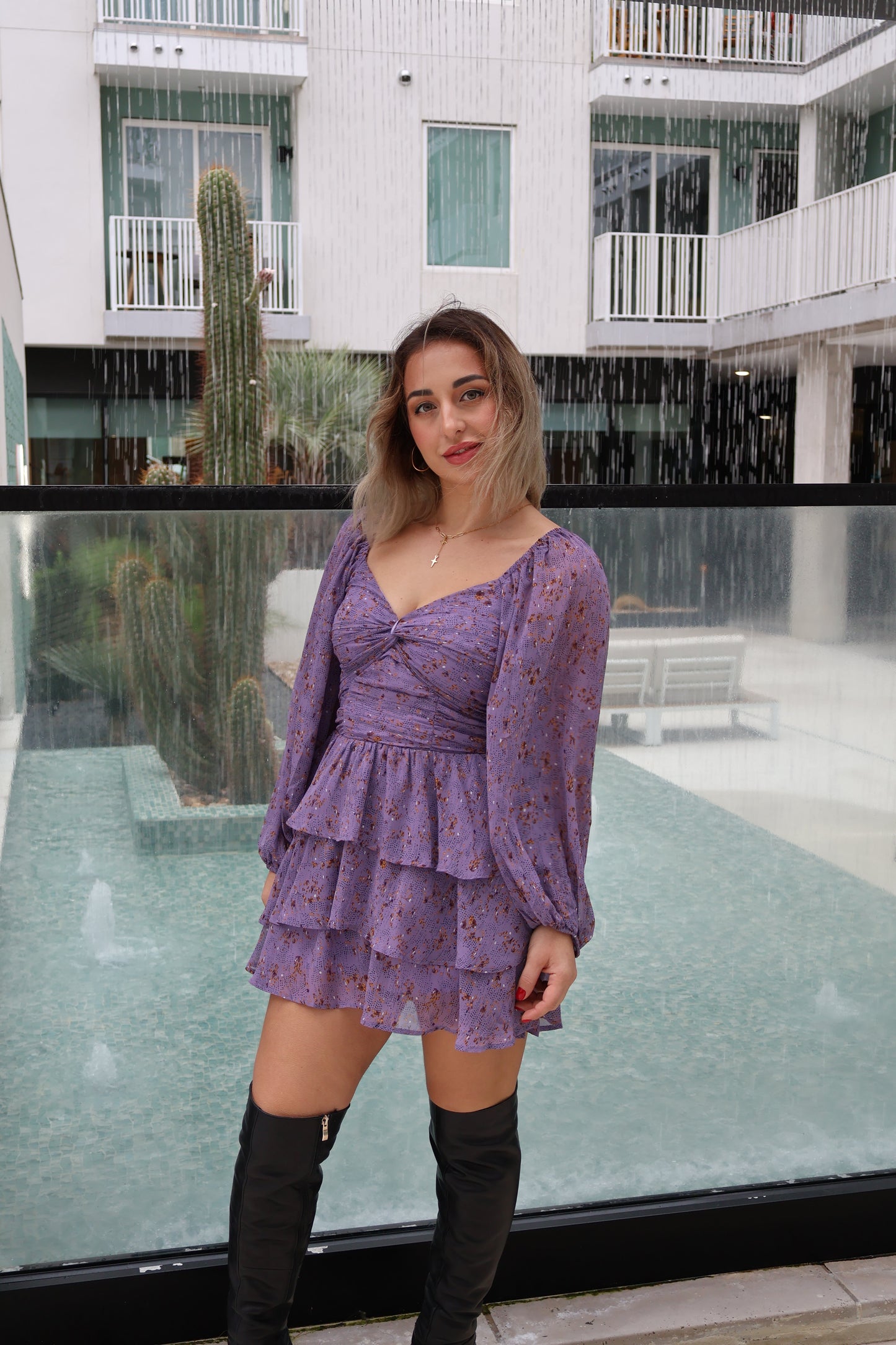 Woman in a purple dress standing in front of a modern building with glass walls.