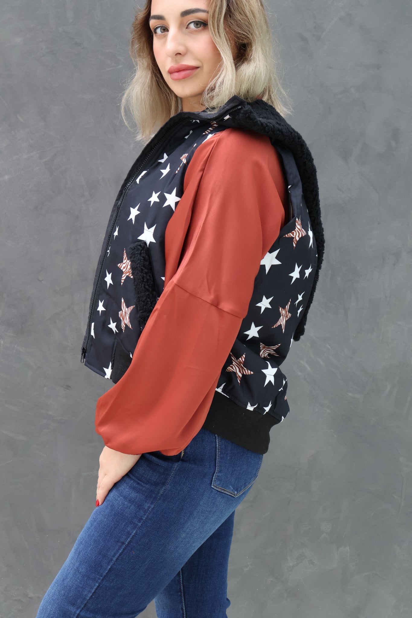 Woman wearing a black jacket with star pattern and red sleeves against a gray background