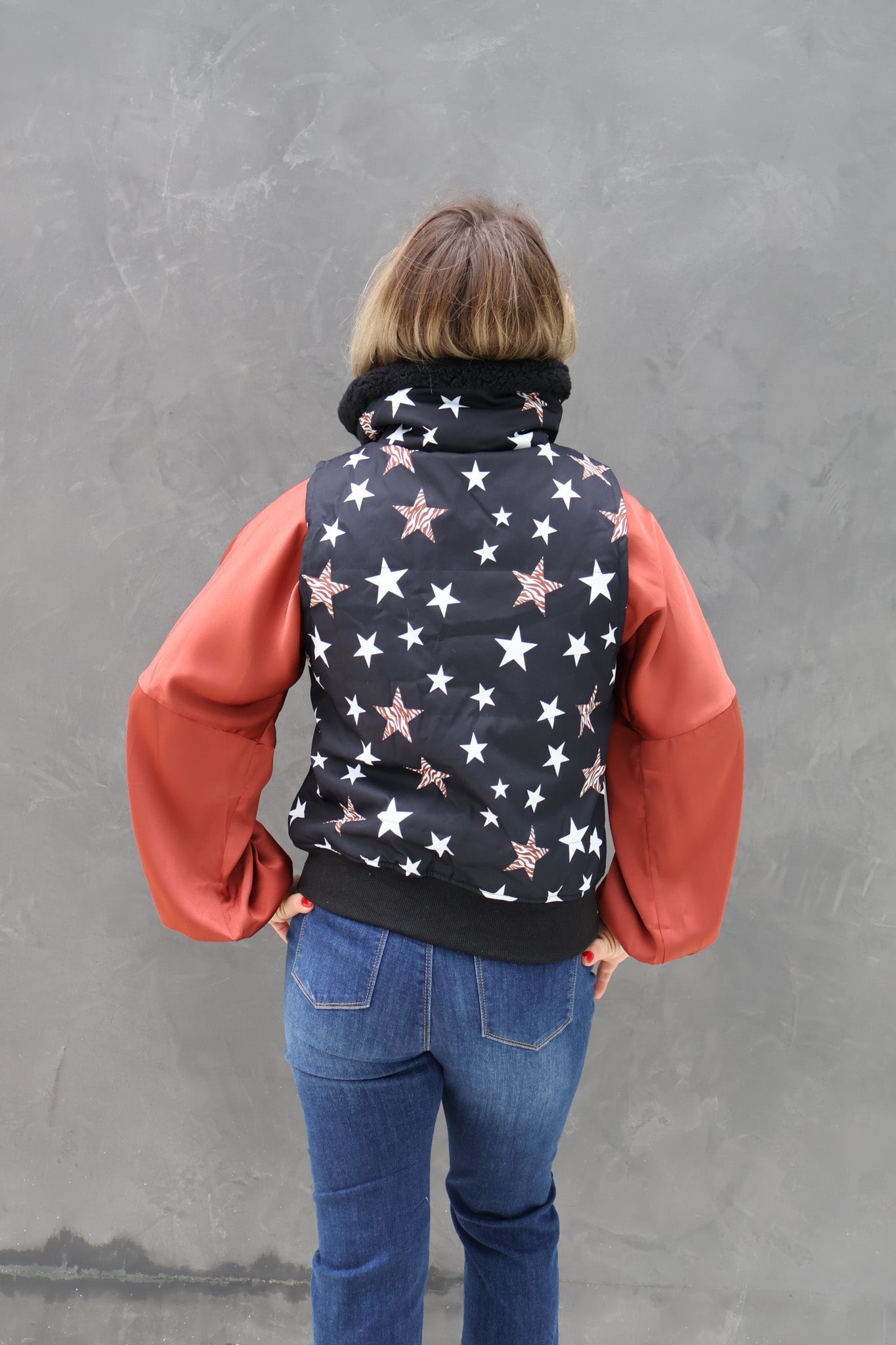 Person wearing a star-patterned vest over a red shirt with blue jeans against a gray background