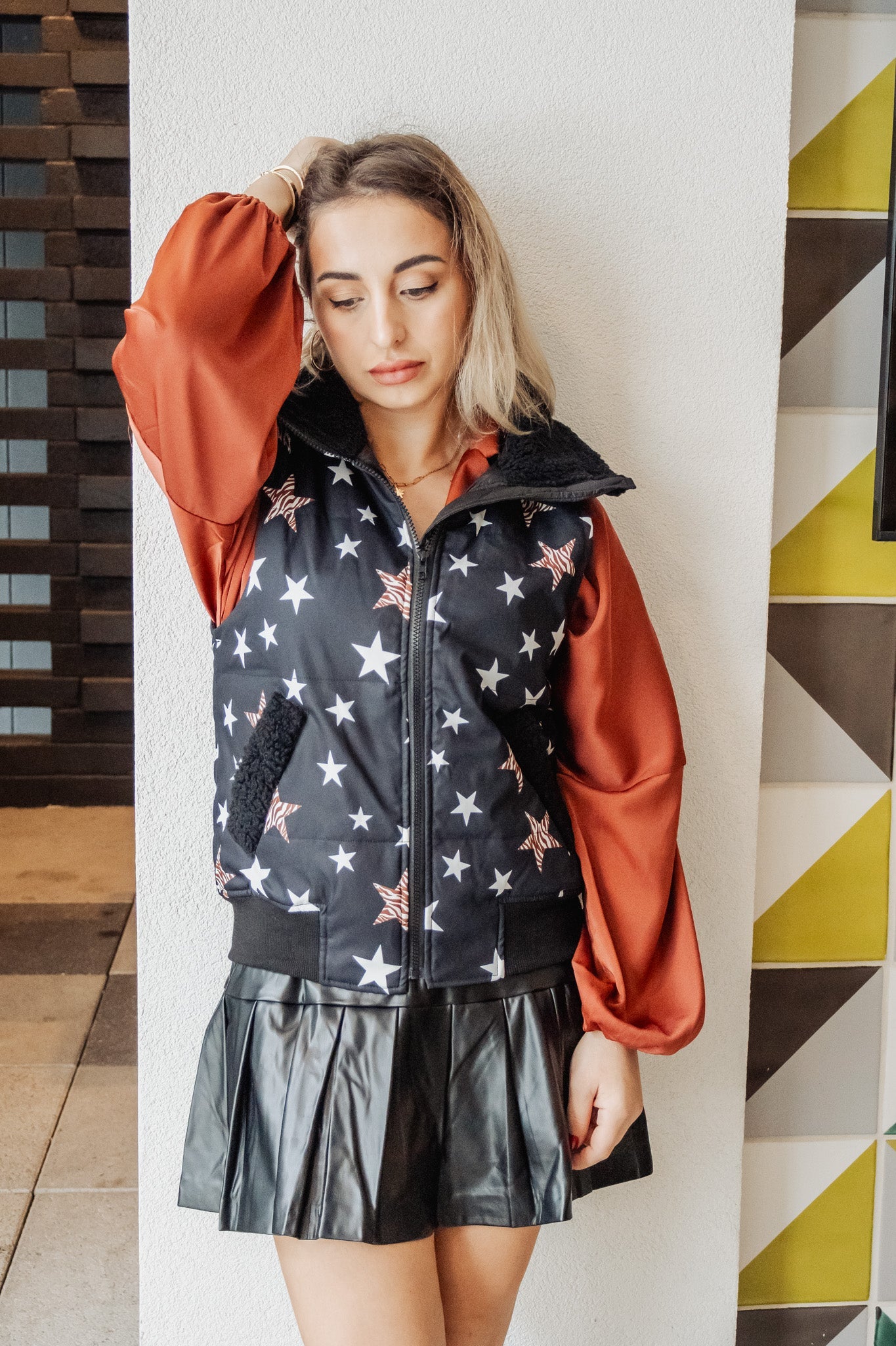 Woman wearing a star-patterned vest over a red hoodie with a geometric wall in the background