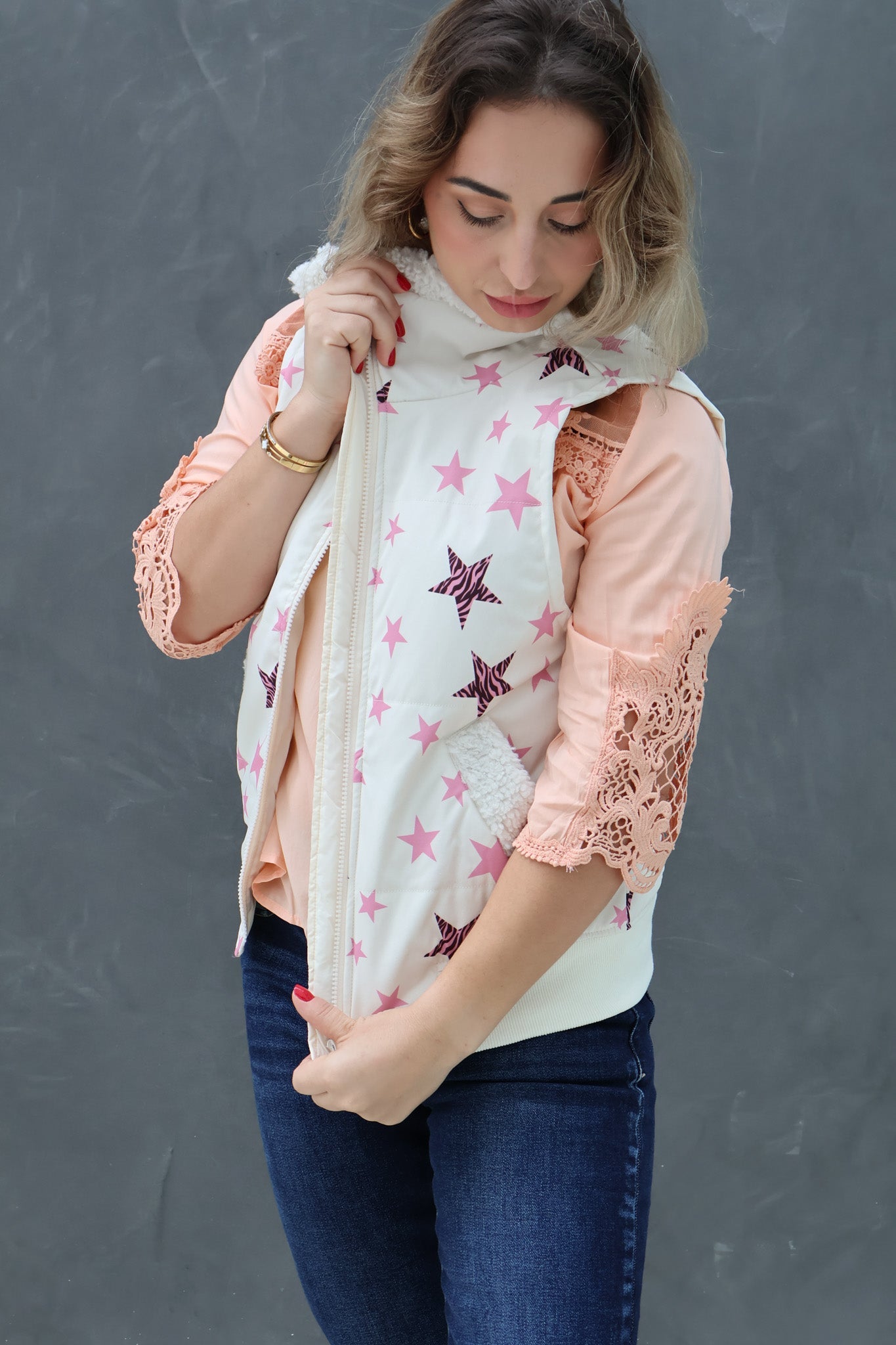 Woman wearing a pink blouse with lace sleeves and a star-patterned vest against a gray background