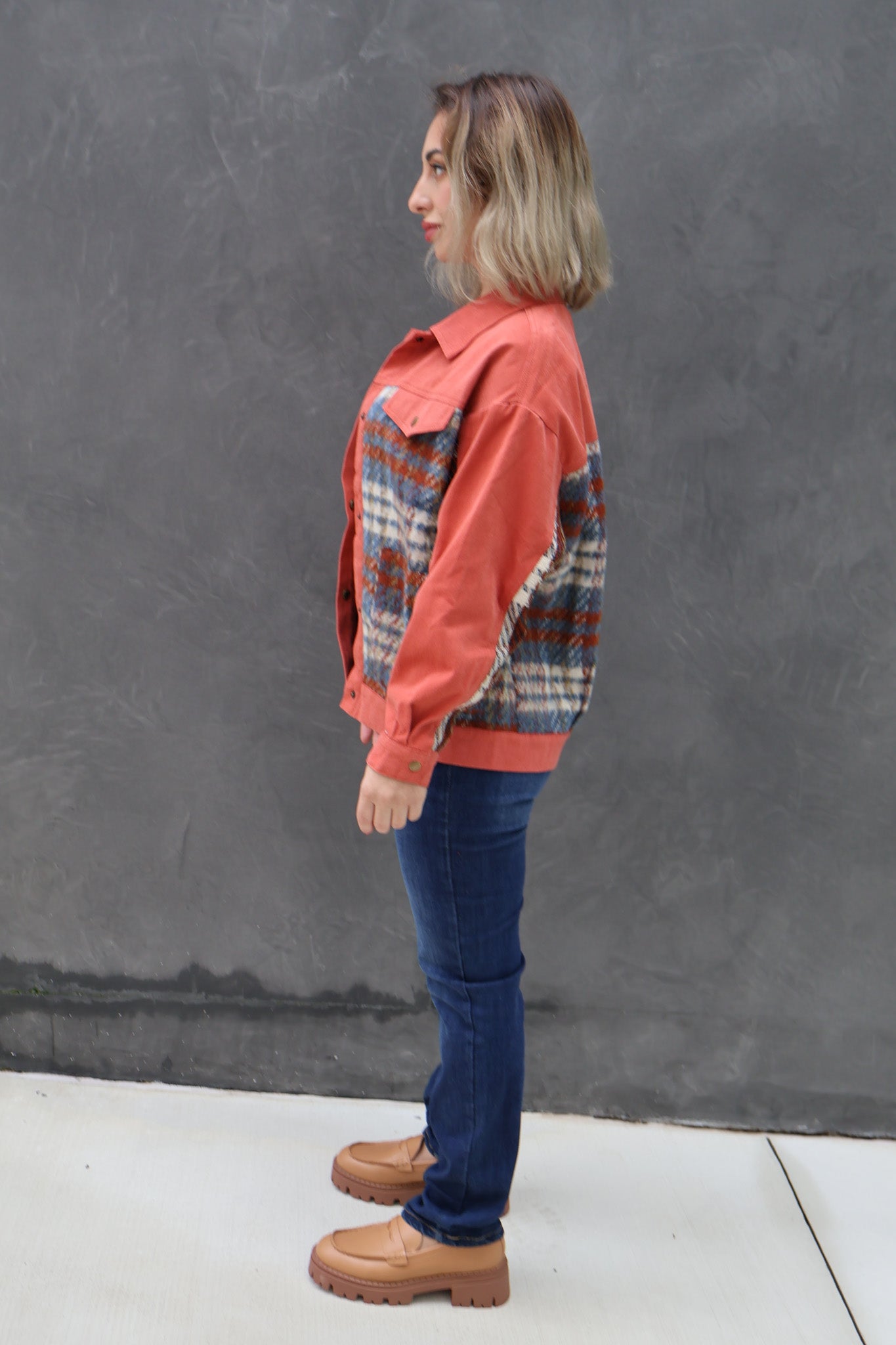 Person wearing a colorful jacket and blue jeans against a gray wall.