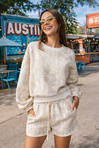 Woman in a matching beige outfit with sunglasses standing in an urban setting with 'Austin' sign in the background.