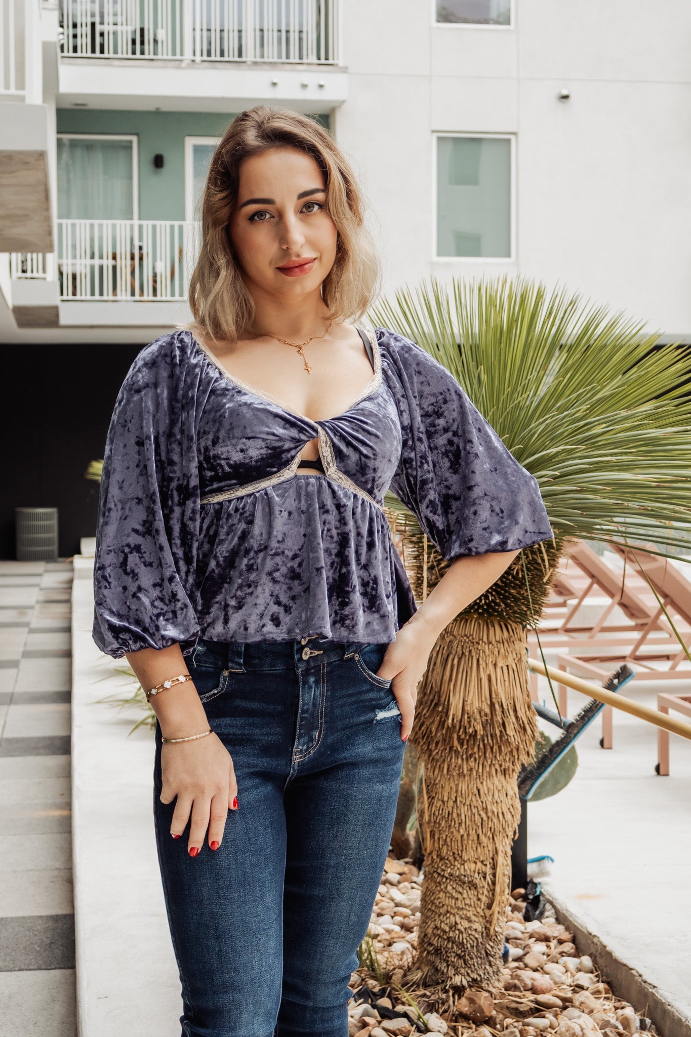 Woman wearing a purple velvet top and blue jeans standing outdoors.