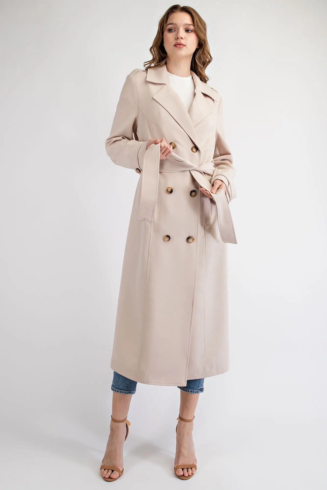 The double-breasted front features large buttons for a traditional look, while the notched lapel and belted waist add to the elegant silhouette. The coat has two side pockets for added convenience and a back vent for ease of movement.