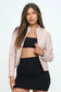 baby pink Moto jacket with a zipper opening. the jacket has side zippers. The model is styling the jacket with a black crop top and black skirt. 